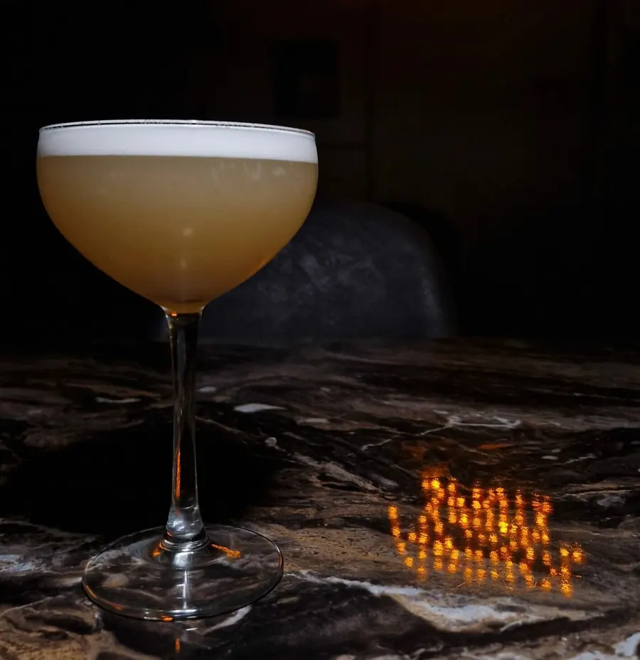 Cocktail sour devant l’enseigne lumineuse du bar